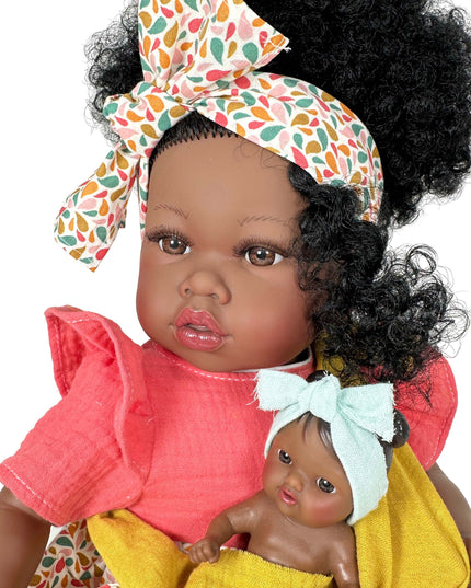 Doll with curly hair wearing a colorful headband, holding another smaller doll wrapped in yellow fabric.