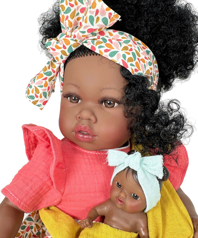 Doll with curly hair wearing a colorful headband, holding another smaller doll wrapped in yellow fabric.