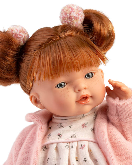 Doll with red hair styled in buns, wearing a pink outfit on a white background