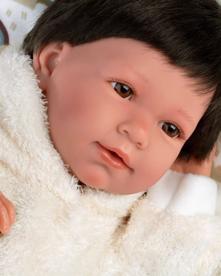 Realistic baby doll with dark hair and brown eyes, wrapped in a white blanket on a patterned background.