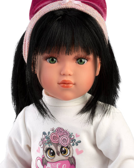 Doll with black hair and a pink headband wearing a white shirt with a owl design.