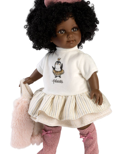Doll with black hair wearing a white shirt with a penguin design, beige skirt, pink socks, and holding a pink bag on a white background.