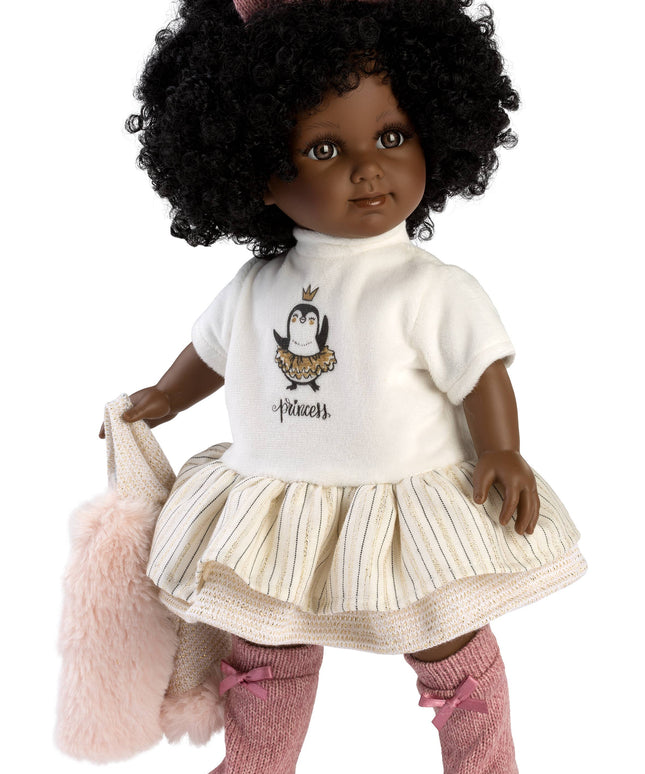 Doll with black hair wearing a white shirt with a penguin design, beige skirt, pink socks, and holding a pink bag on a white background.