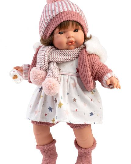 Doll wearing a pink knitted hat, scarf, and socks on a white background