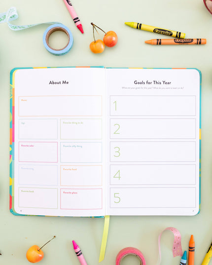 Open planner with 'About Me' and 'Goals for This Year' sections on a colorful background with stationery items.