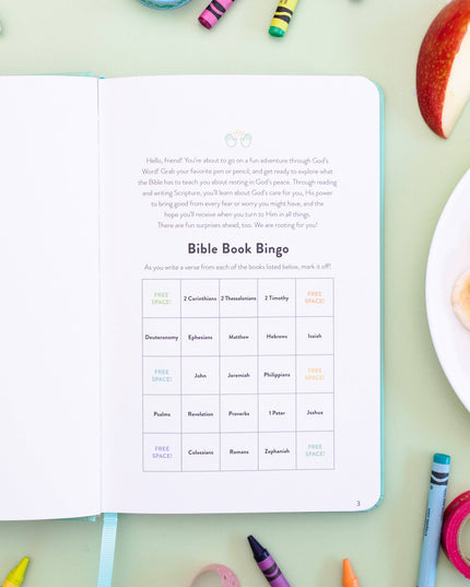 Open book with Bible Book Bingo worksheet on a table with snacks and crayons