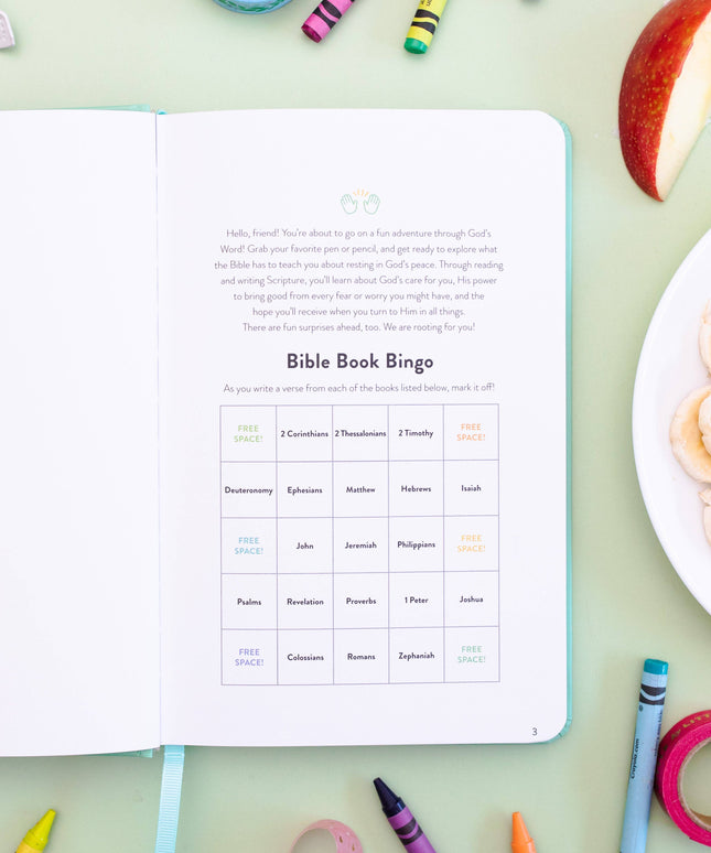Open book with Bible Book Bingo worksheet on a table with snacks and crayons