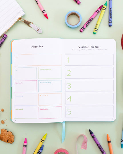 Open planner with 'About Me' and 'Goals for This Year' sections on a table with crayons and snacks.