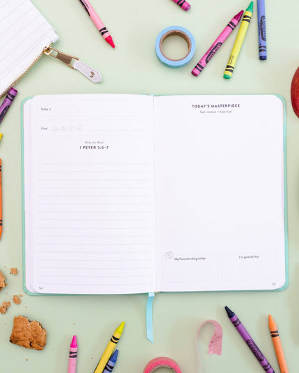 Open notebook with inspirational text surrounded by colorful crayons and stationery on a light green background