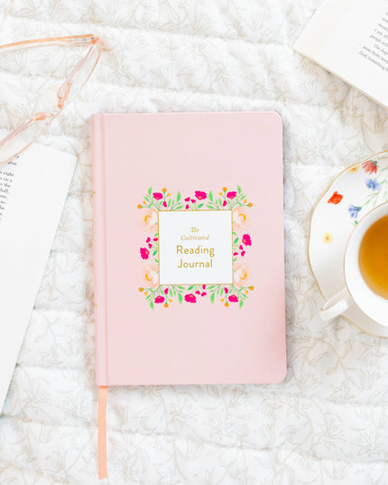 Pink reading journal with floral design on a white surface with a teacup.