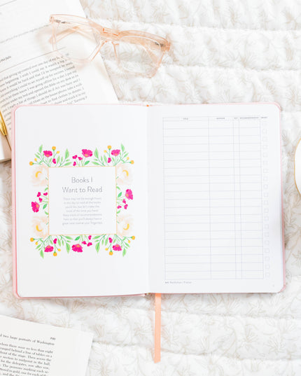 Open notebook with floral design on a white surface with books and glasses.