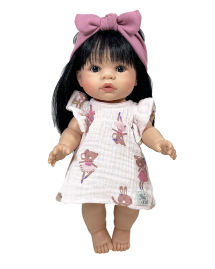 Doll with black hair and a pink bow wearing a white dress with pink patterns on a white background