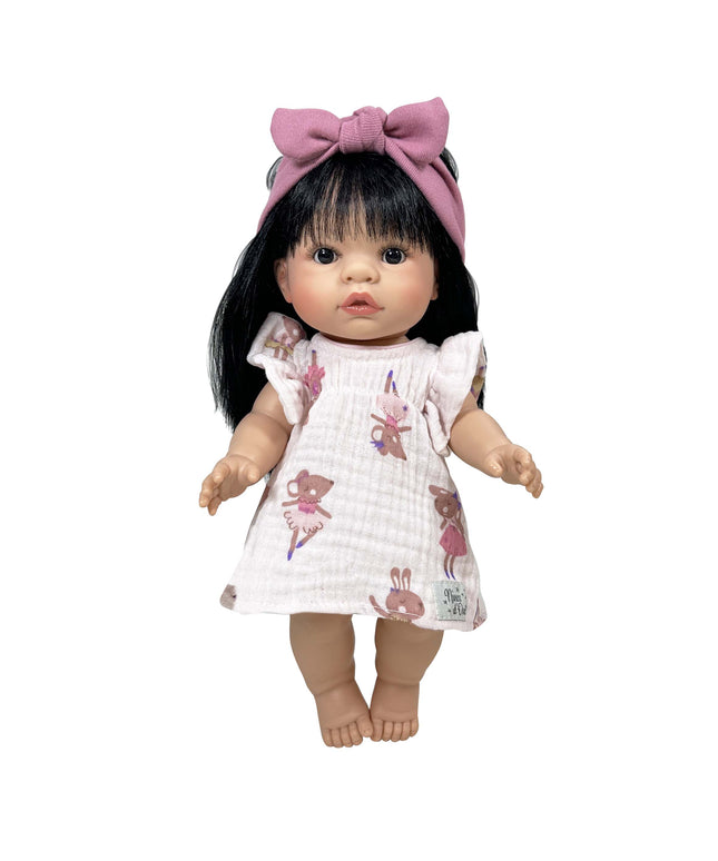 Doll with black hair and a pink bow wearing a white dress with pink patterns on a white background