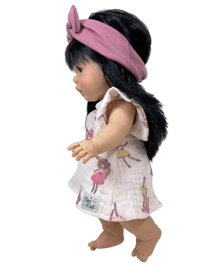 Doll wearing a pink headband and a white dress with printed designs on a white background