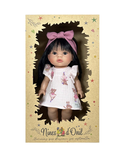 Doll in a box with a pink bow, wearing a white dress with floral patterns, on a beige background with 'Nines d'Oril' branding.