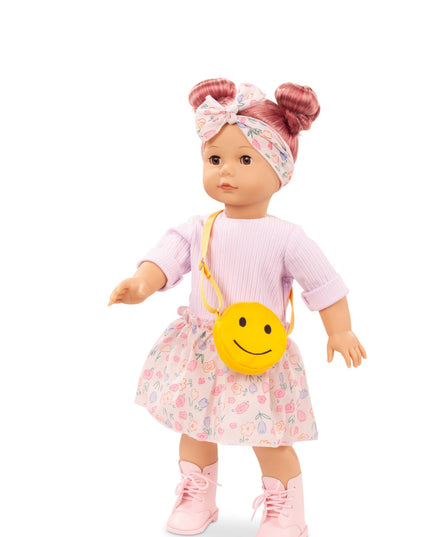 Doll wearing a pink outfit with a floral skirt and yellow smiley face bag on a white background