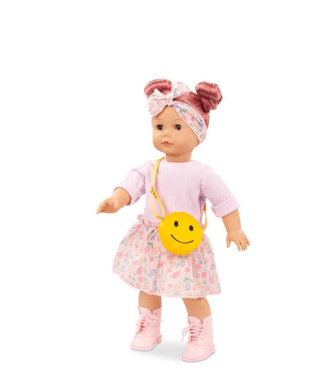 Doll wearing a pink outfit with a floral skirt and yellow smiley face bag on a white background