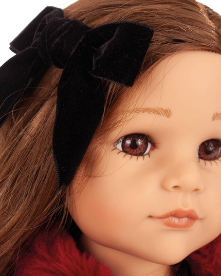 Close-up of a doll with brown hair and a black bow, wearing a red garment.