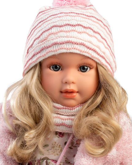 Doll wearing a pink striped hat with a pom-pom and a matching pink coat on a white background