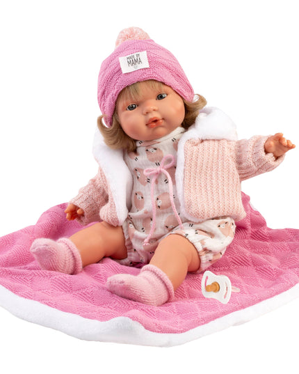 Baby doll in pink outfit with matching hat on a pink blanket against a white background