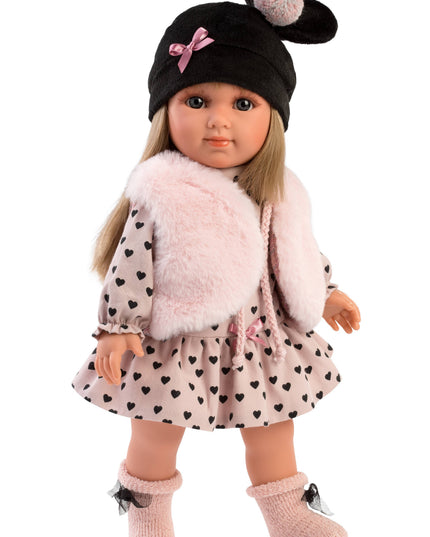 Doll wearing a black hat with pom-poms, pink fluffy sweater, and polka dot dress on a white background