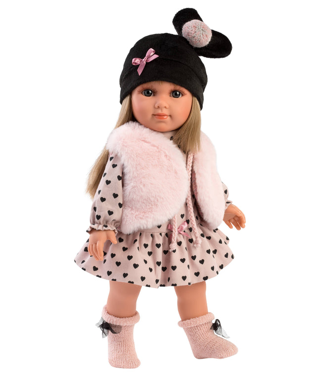 Doll wearing a black hat with pom-poms, pink fluffy sweater, and polka dot dress on a white background