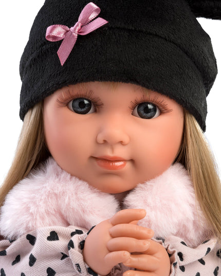 Doll wearing a black hat with a pink bow and a pink outfit with black heart patterns.