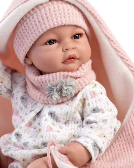 Baby doll wrapped in a pink blanket with a pink outfit and white flowers.