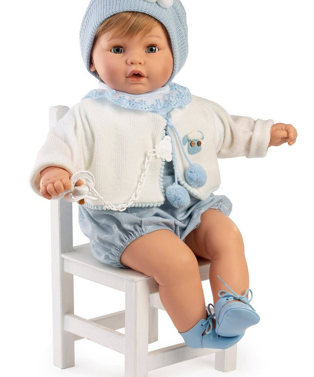 Baby doll in blue outfit sitting on a white chair against a white background