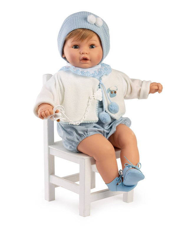 Baby doll in blue outfit sitting on a white chair against a white background