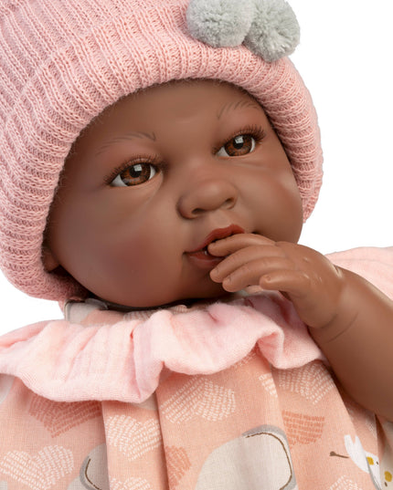Baby doll wearing a pink knitted hat and dress with animal patterns on a white background