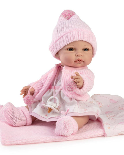 Baby doll in pink outfit with matching hat and blanket on a white background