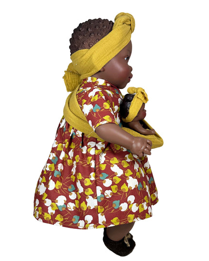 Doll wearing a red dress with floral patterns and a yellow headscarf on a white background