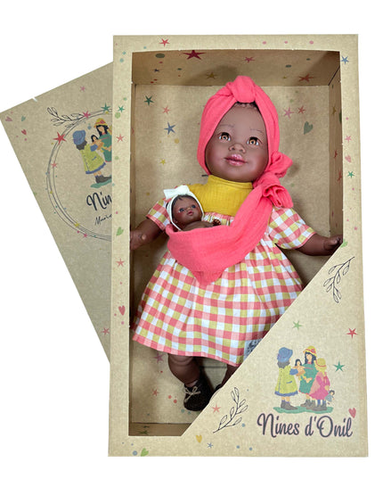 Doll in a red checkered dress and headscarf holding a smaller doll, both in a decorative box with 'Nines d'Oril' branding.