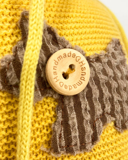 Yellow knitted item with a textured patch and wooden button labeled 'Handmade Quality'.