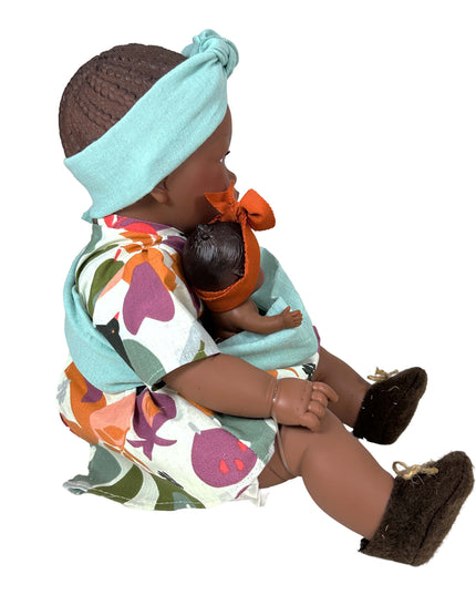 Doll holding a smaller doll with a colorful outfit and headband on a white background