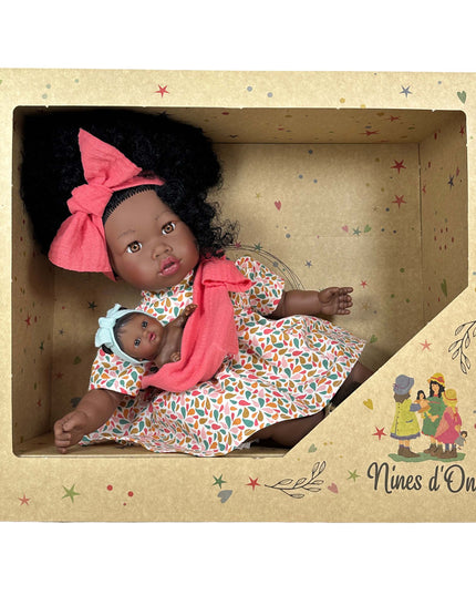 Doll with a baby in a colorful dress and headband, inside a decorated box with 'Nines d'Onil' branding.