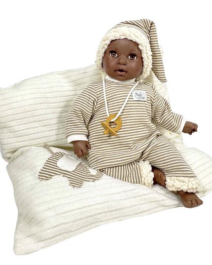 Baby doll in striped outfit sitting on a textured pillow with a white background