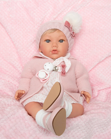 Baby doll in pink outfit with white shoes on a pink textured blanket