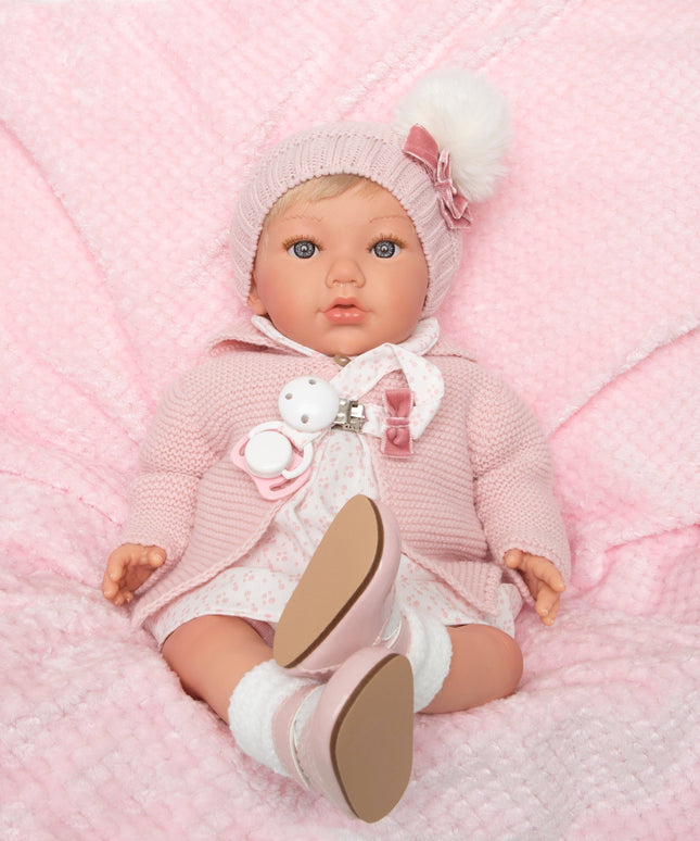Baby doll in pink outfit with white shoes on a pink textured blanket