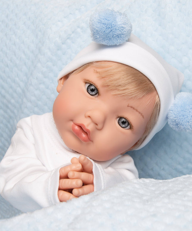 Baby doll with blue eyes and blonde hair wearing a white outfit and blue hat with pom-poms on a light blue textured background.