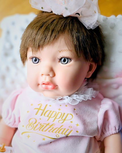 Doll wearing a 'Happy Birthday' shirt on a soft surface