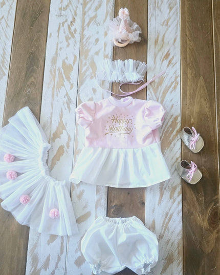 Baby girl's birthday outfit with headband, romper, and shoes on a wooden surface