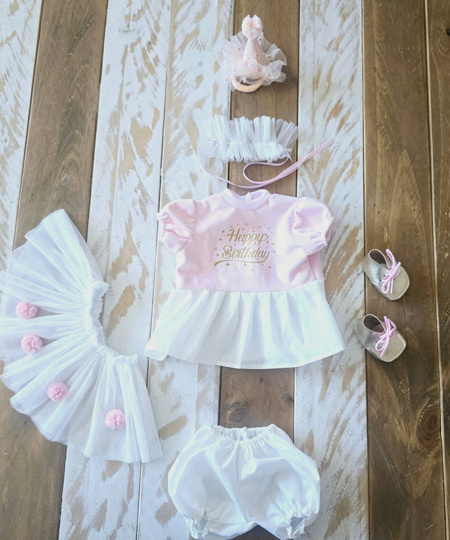 Baby girl's birthday outfit with headband, romper, and shoes on a wooden surface