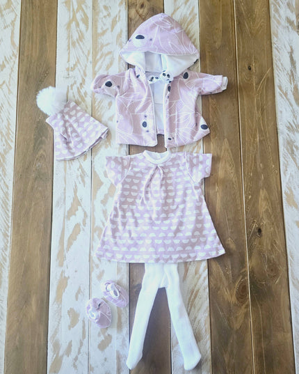 Baby outfit set with pink hooded jacket, dress, and shoes on a wooden surface