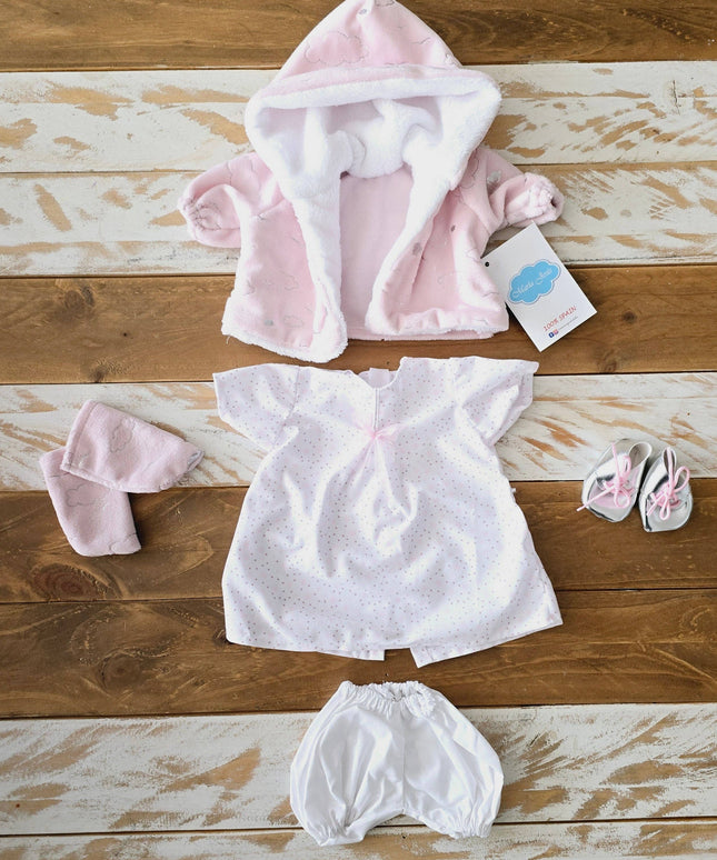 Baby clothing set including a pink hooded jacket, white dress, and bloomers on a wooden surface.