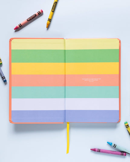 Colorful striped notebook with crayons and pencils on a light blue background