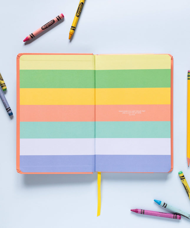 Colorful striped notebook with crayons and pencils on a light blue background