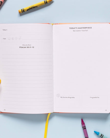 Open notebook with prompts on a light blue background with colorful crayons and pencils.