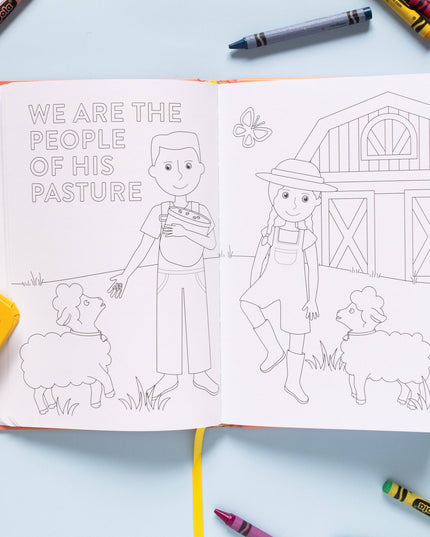 Coloring book open to a page with two children and sheep, surrounded by crayons on a light blue background.